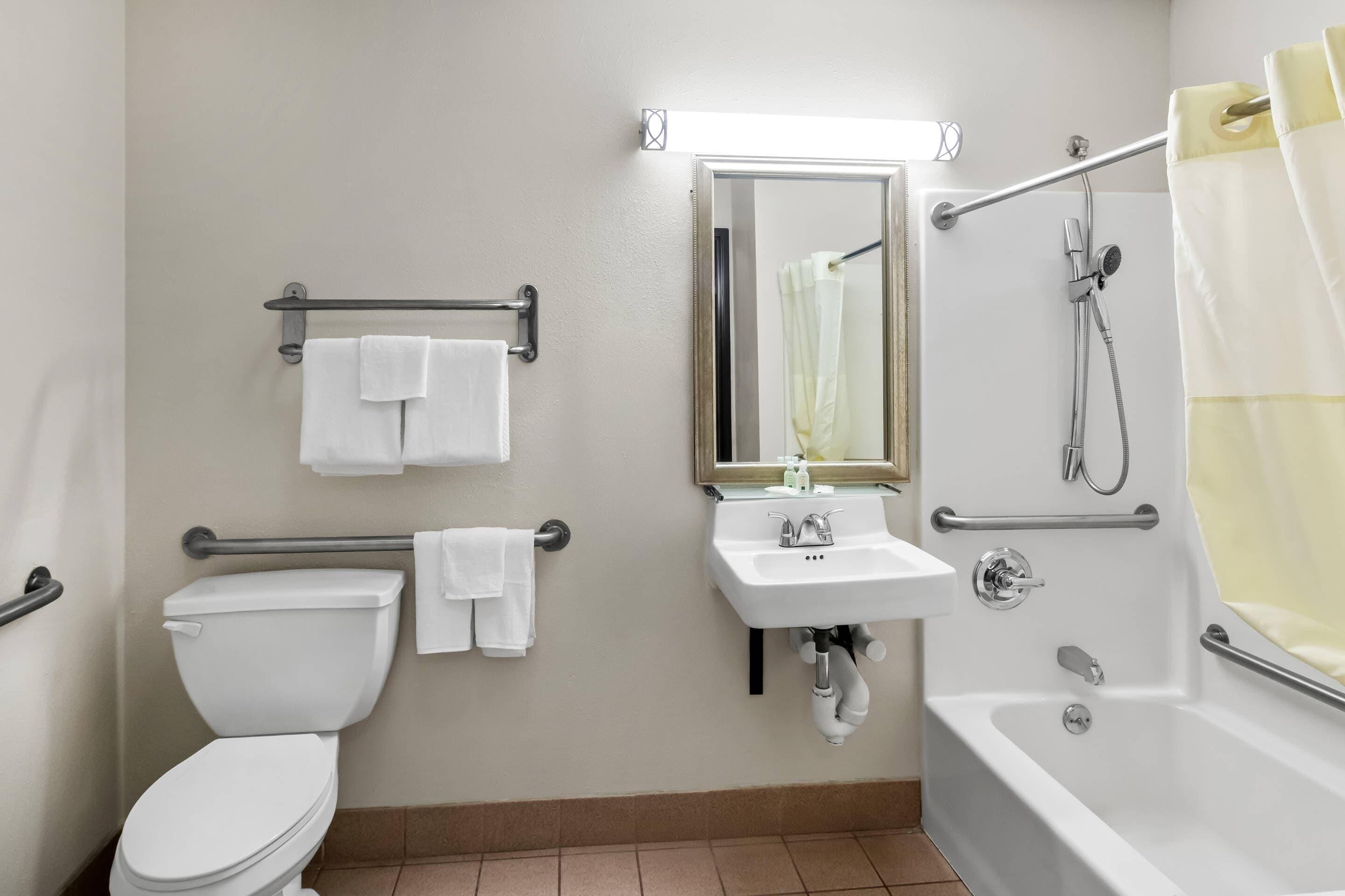 A bathroom with a toilet, sink, and bathtub, equipped with grab bars and a shower curtain.