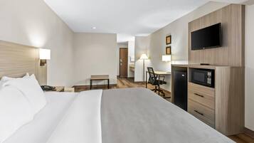 A hotel room with a large bed, a desk with a chair, a television, and a microwave.