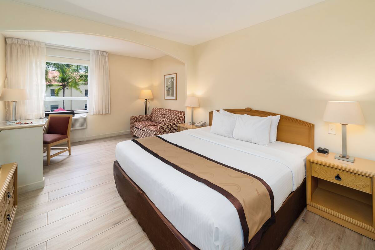 A hotel room with a large bed, a desk, a chair, and a window with curtains.