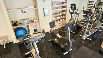 A gym with various exercise machines, a blue exercise ball, and shelves with towels.