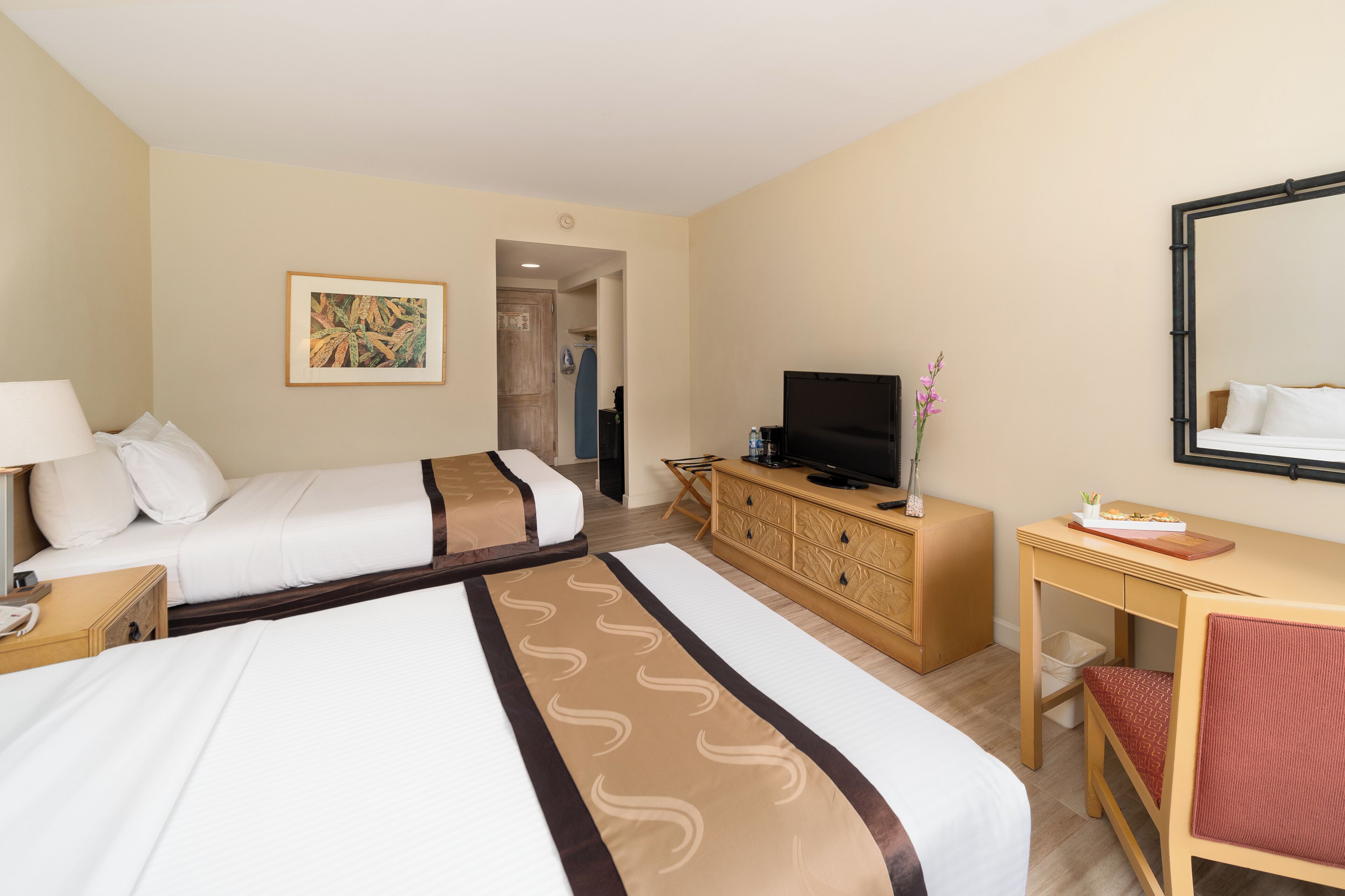 Une chambre d’hôtel avec deux lits, un bureau, une télévision et un miroir.
