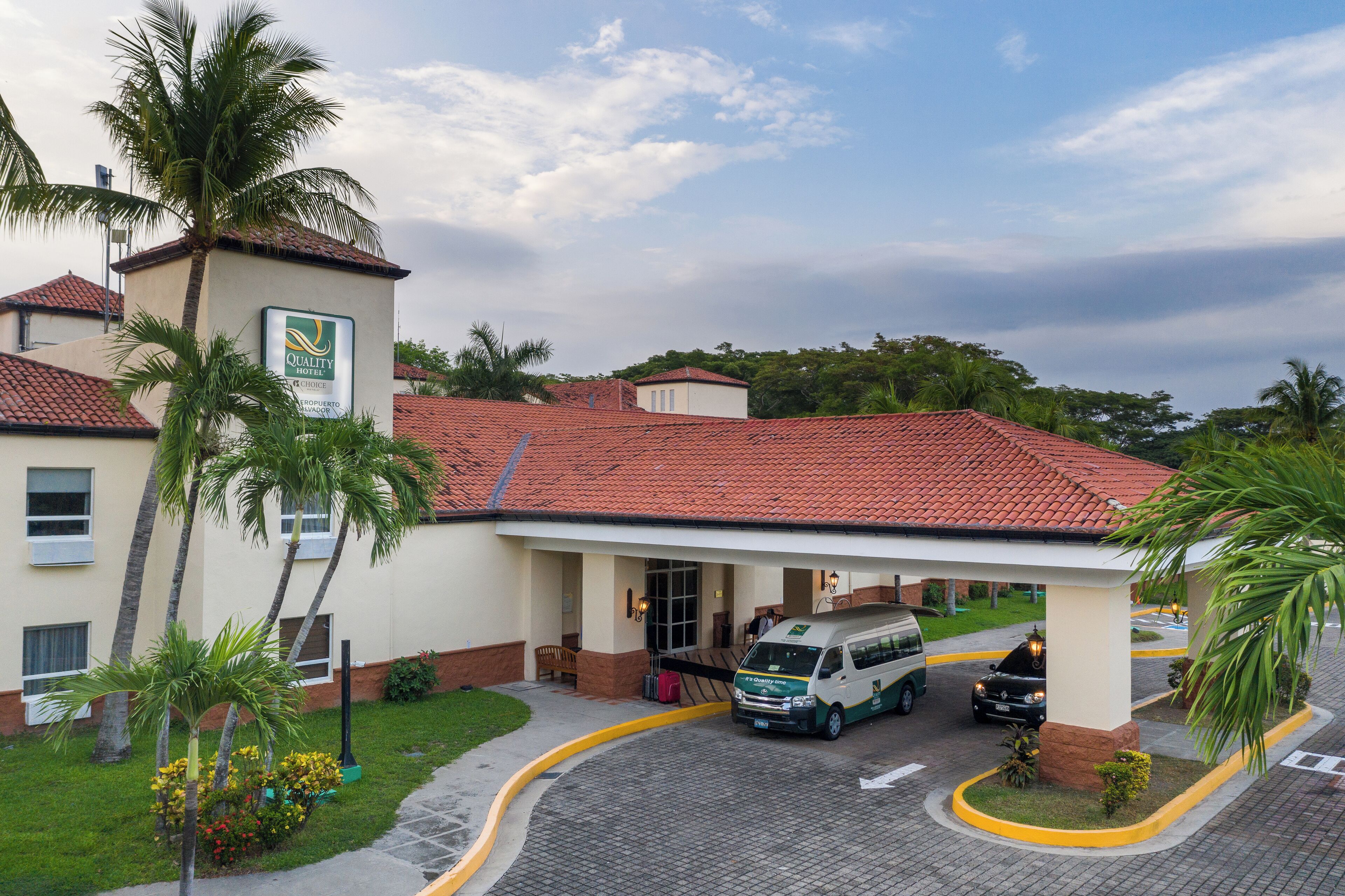 Un hotel con techo de tejas rojas, entrada cubierta y una palmera en primer plano.