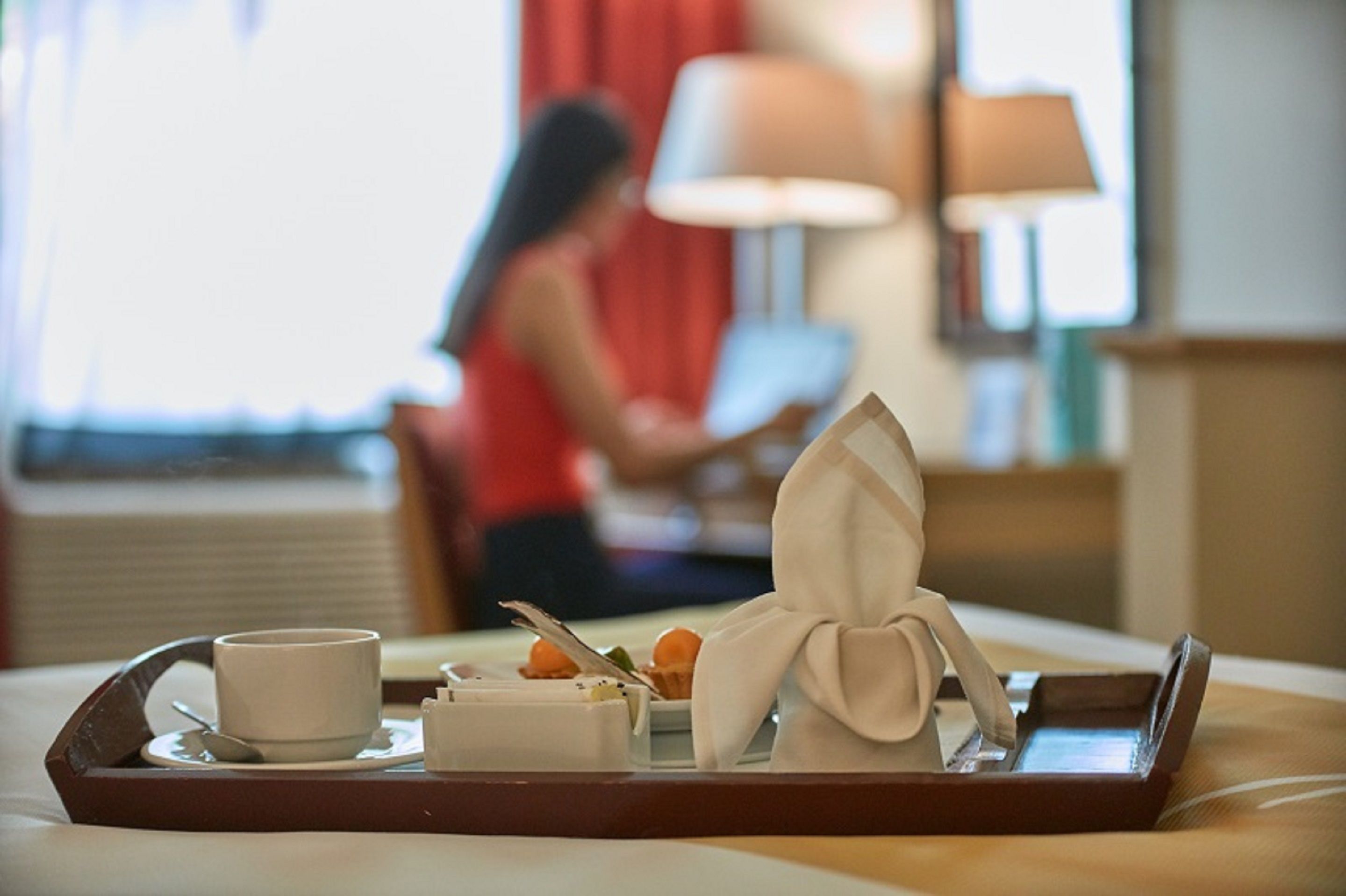 Ett bricka med en kopp, en liten skål och en vikt servett står på ett bord i ett hotellrum.
