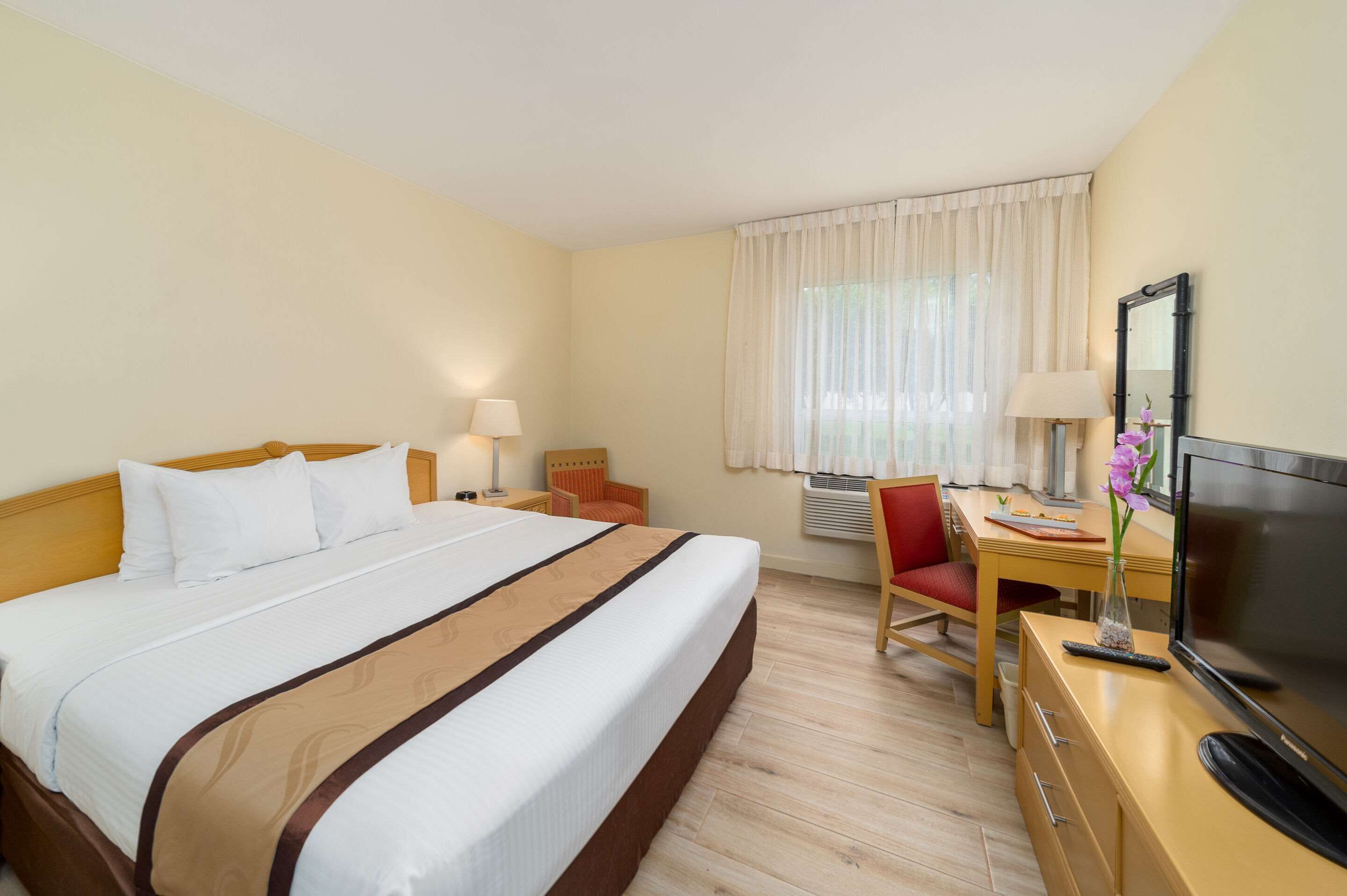 Una habitación de hotel con una cama grande, un escritorio con silla, televisión y ventana con cortinas.
