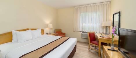 Une chambre d’hôtel avec un grand lit, un bureau avec une chaise, une télévision et une fenêtre avec des rideaux.