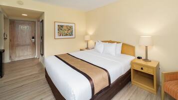 Habitación de hotel con una cama grande, dos mesitas de noche con lámparas, una silla de madera y una puerta que da a otra habitación.