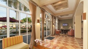 A hotel lobby with a checkered floor, a sofa with patterned cushions, a potted plant, and a television mounted on the wall. - Quality Hotel Real Aeropuerto (San Luis Talpa)