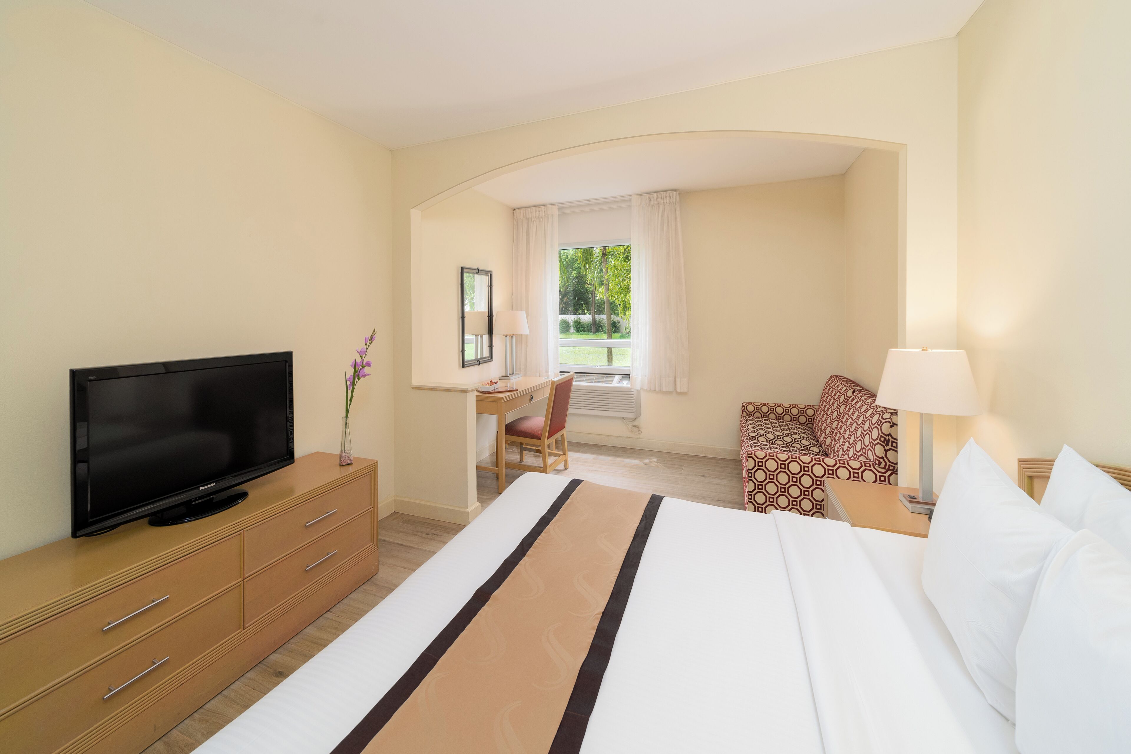 A hotel room with a bed, a TV, a desk, and a chair.