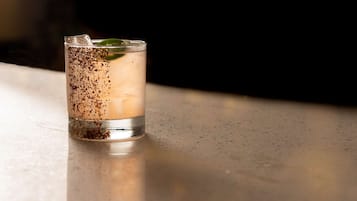A clear glass with a beverage, ice cubes, and a mint leaf on a reflective surface.