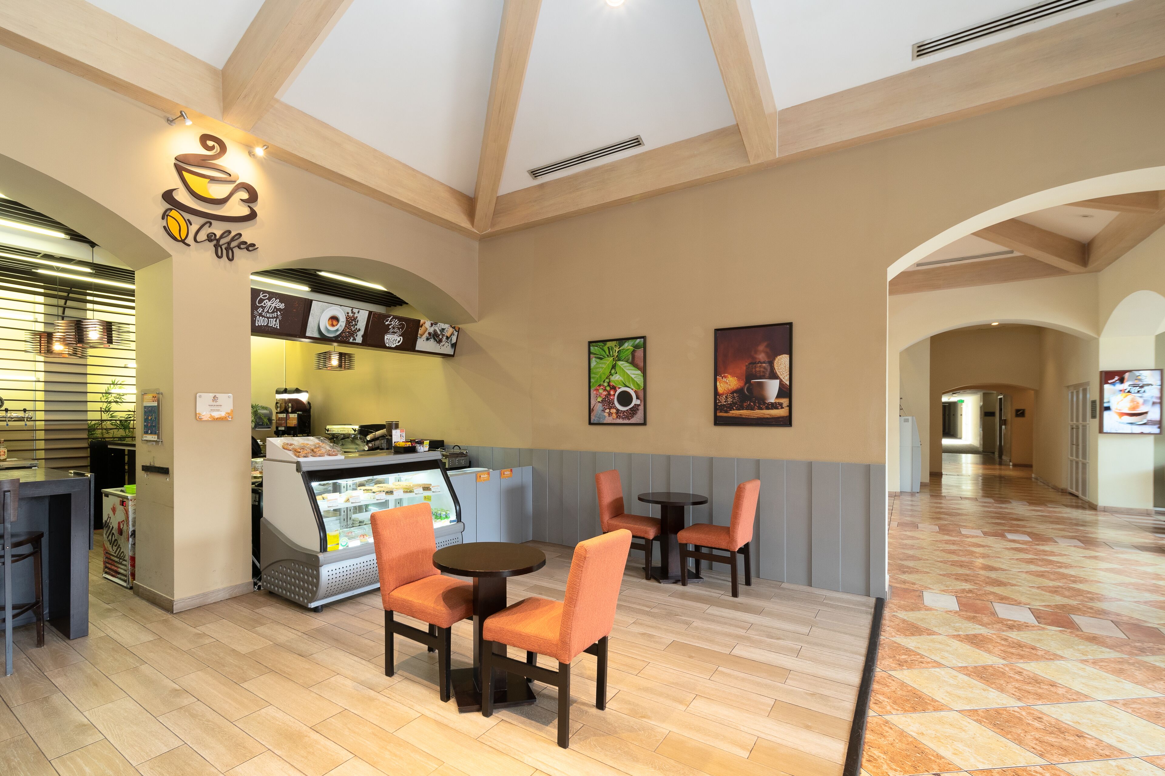 A café with a modern interior, featuring a coffee machine, seating area with tables and chairs, and a display case with food items.