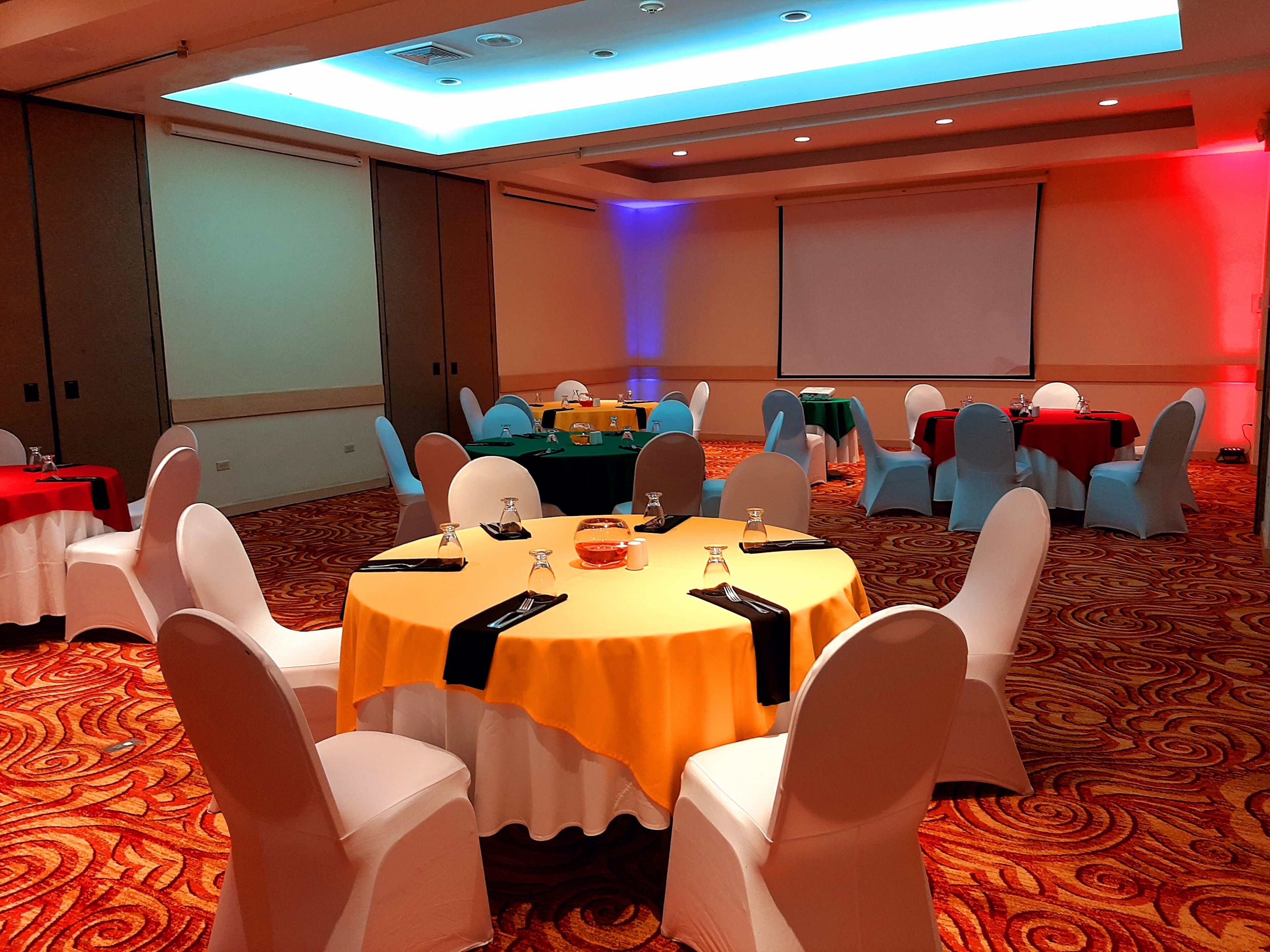 Une salle de conférence avec des tables rondes, des chaises blanches et un sol recouvert de moquette.