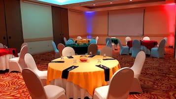 Une salle de conférence avec des tables rondes, des chaises blanches et un sol recouvert de moquette.