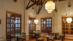 A dining area with wooden tables and chairs, large windows with multiple panes, and hanging pendant lights. - Quality Hotel Real Aeropuerto (San Luis Talpa)
