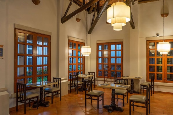A dining area with wooden tables and chairs, large windows with multiple panes, and hanging pendant lights. - Quality Hotel Real Aeropuerto (San Luis Talpa)