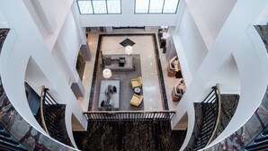 Un moderno vestíbulo de hotel con un área de estar central, una escalera y vistas al piso superior.