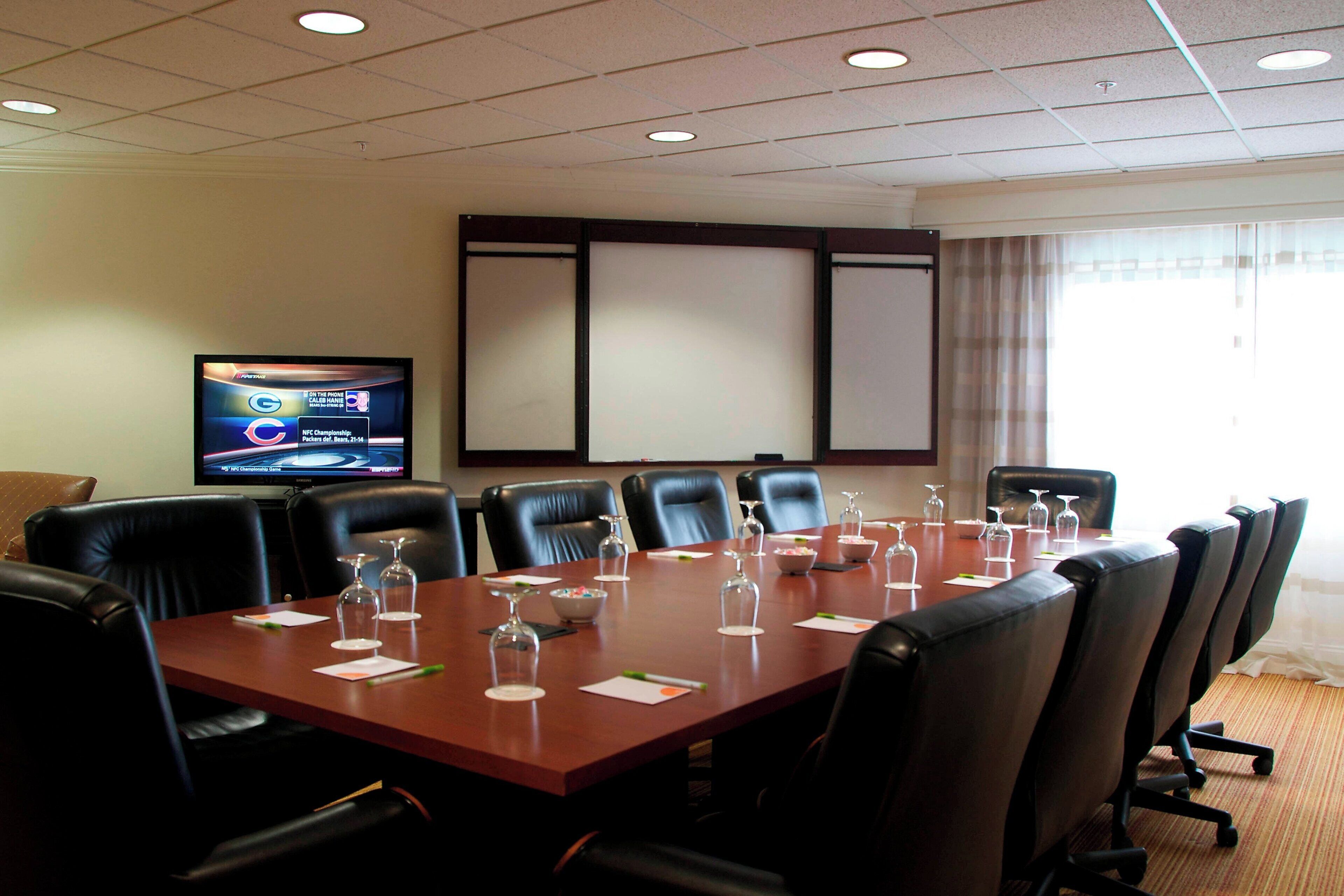 Un salón de conferencias con una larga mesa, sillas de cuero negro y una televisión en la pared.