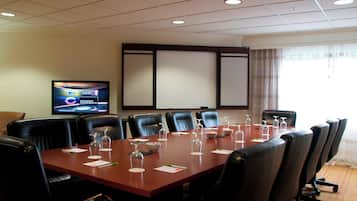 Un salón de conferencias con una larga mesa, sillas de cuero negro y una televisión en la pared.