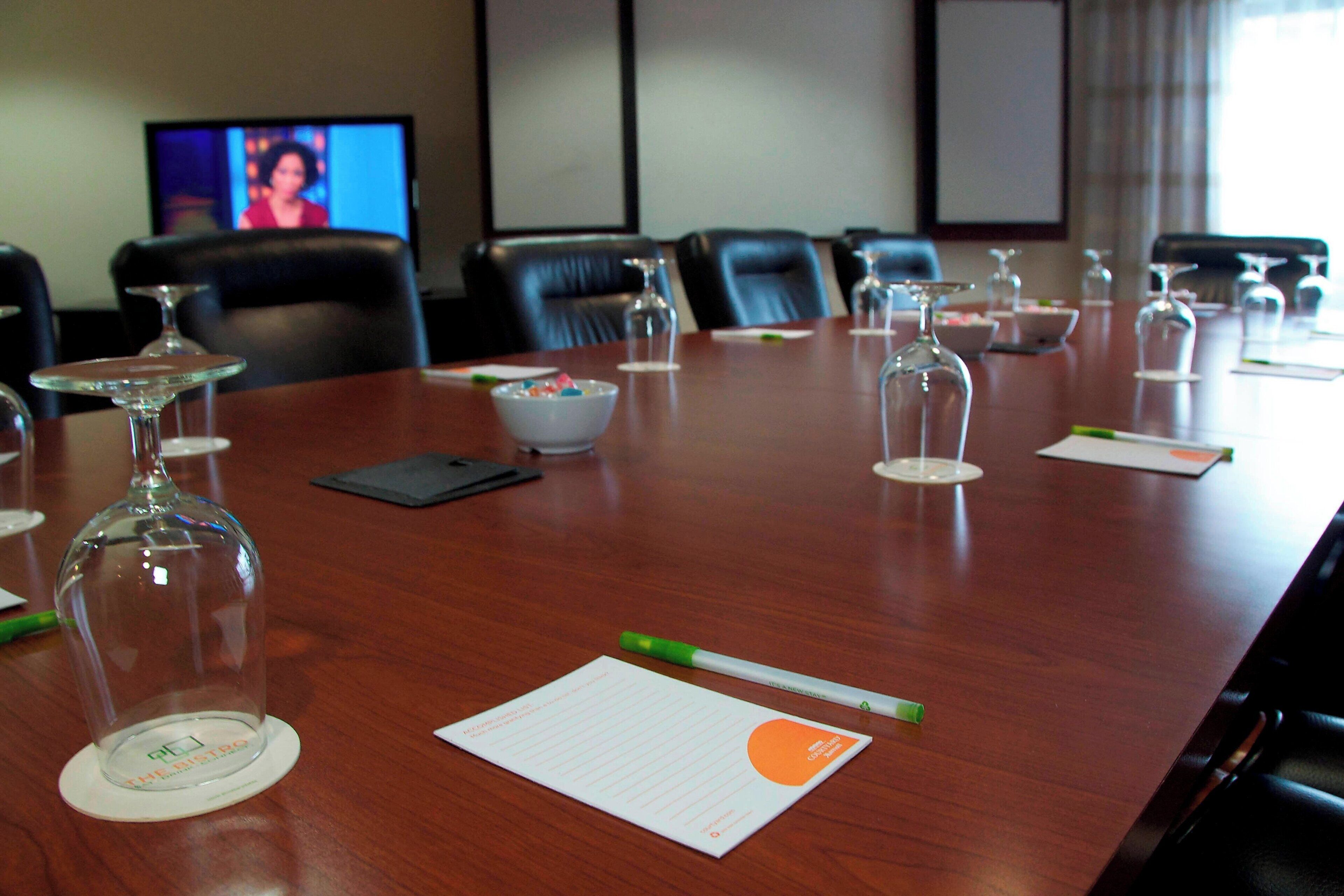 Un salón de conferencias con una mesa larga, sillas, un televisor y un tazón de cereal.