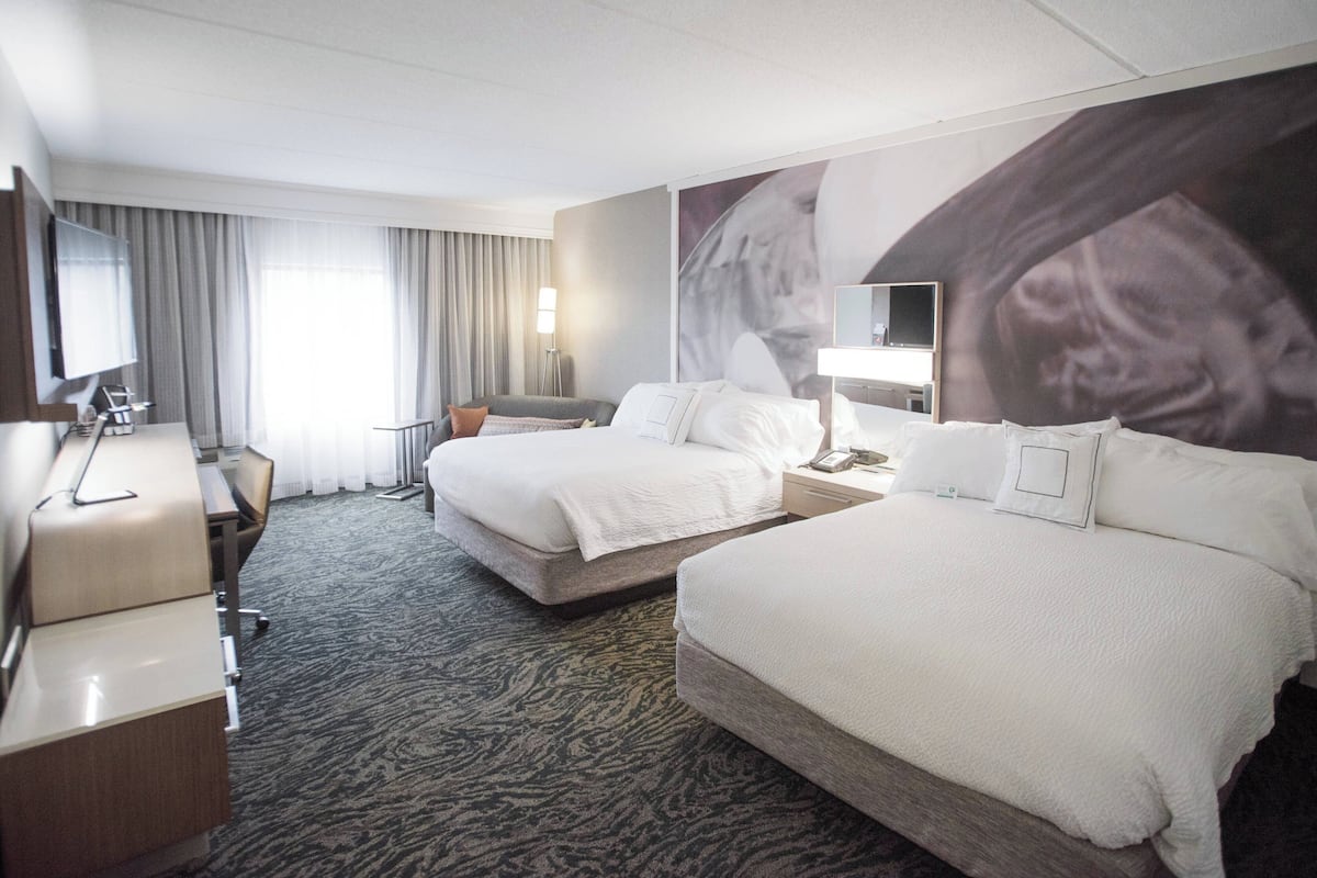 A hotel room with two beds, a desk, a chair, a TV, and a large wall mural.