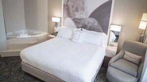 Habitación de hotel con una cama grande, baño independiente con bañera, una silla y dos lámparas de noche.