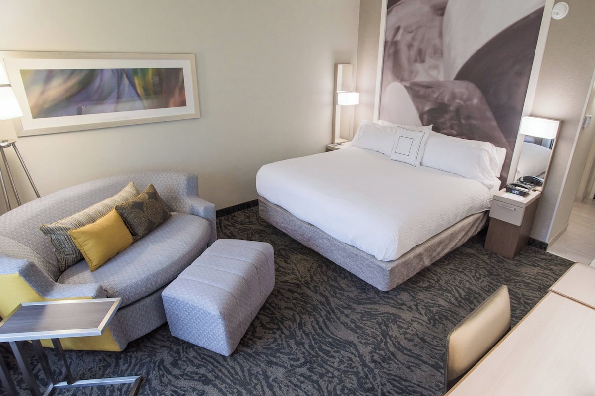 A hotel room with a bed, a sofa, a small table, and a lamp.