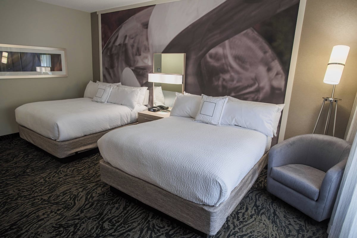 A hotel room with two beds, a desk, a chair, a lamp, and a large wall mural.
