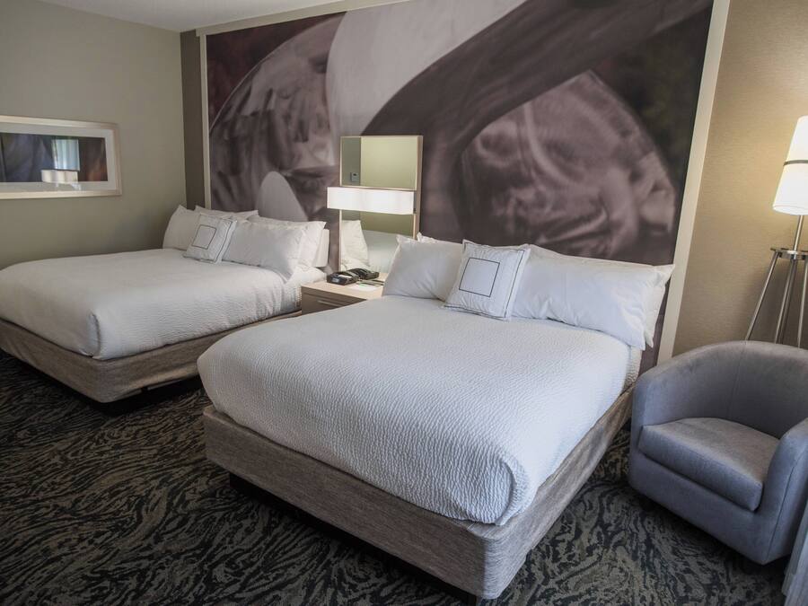 Een hotelkamer met twee bedden, een bureau, een stoel, een lamp en een groot wanddecor.