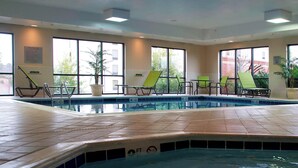 Una piscina con sillas de descanso, ventanas amplias y suelo de baldosas.