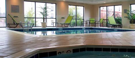 Una piscina con sillas de descanso, ventanas amplias y suelo de baldosas.