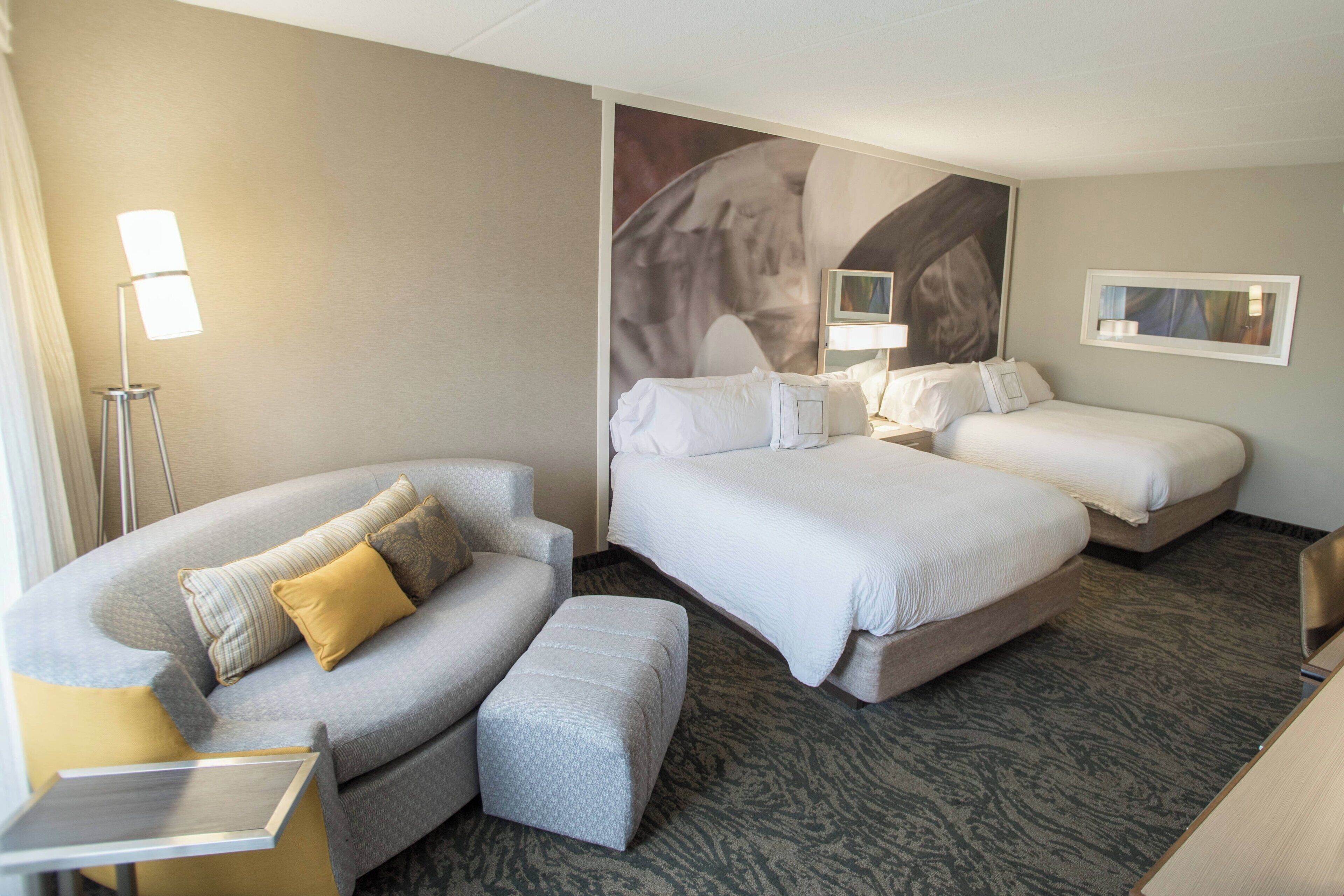 Een hotelkamer met een bank, twee bedden, een kleine tafel en een vloerlamp.