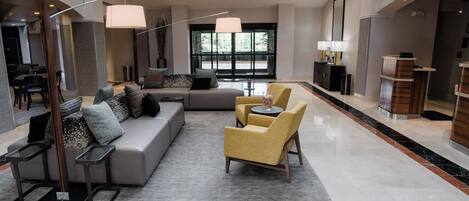 A spacious lobby with a grey sofa, yellow armchairs, a coffee table, and a large window.