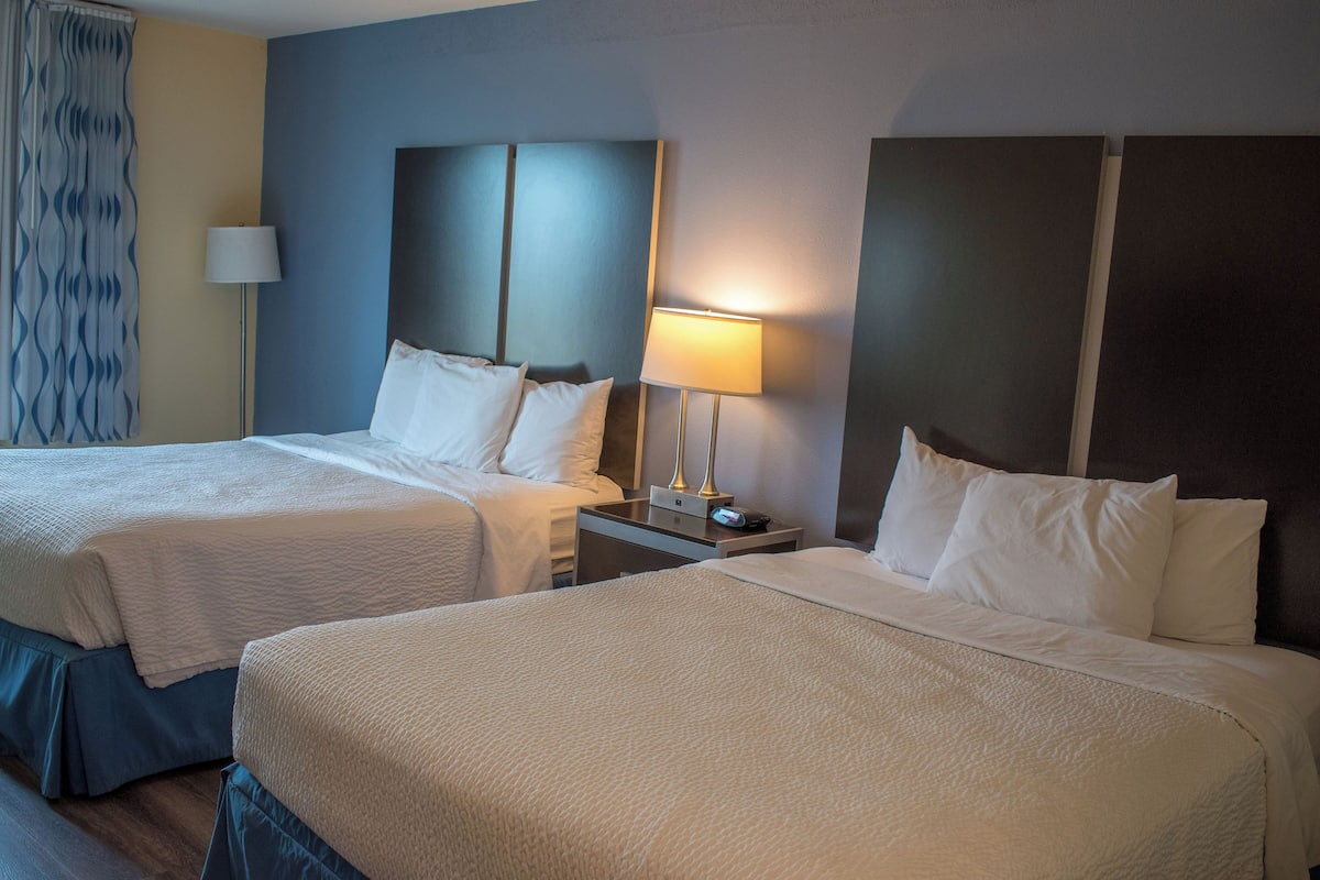 A hotel room with two beds, a nightstand with a lamp, and a patterned curtain.