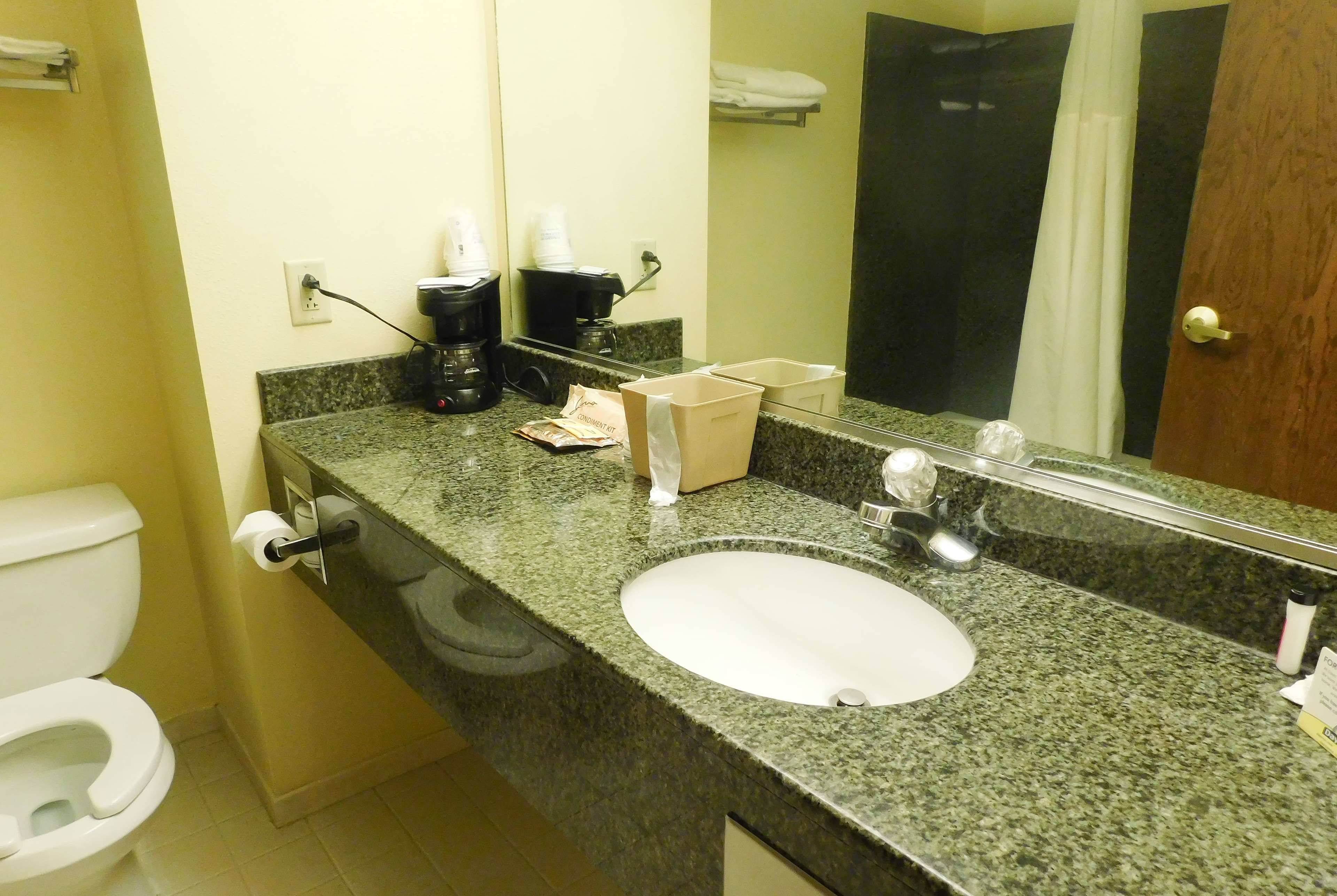 A bathroom with a white sink, a mirror, a toilet, and a coffee maker.