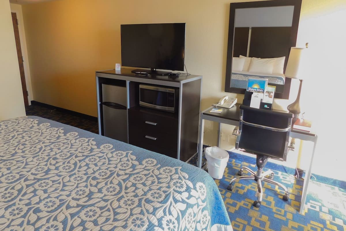 A hotel room with a bed, a desk with a telephone, a television, and a mirror.