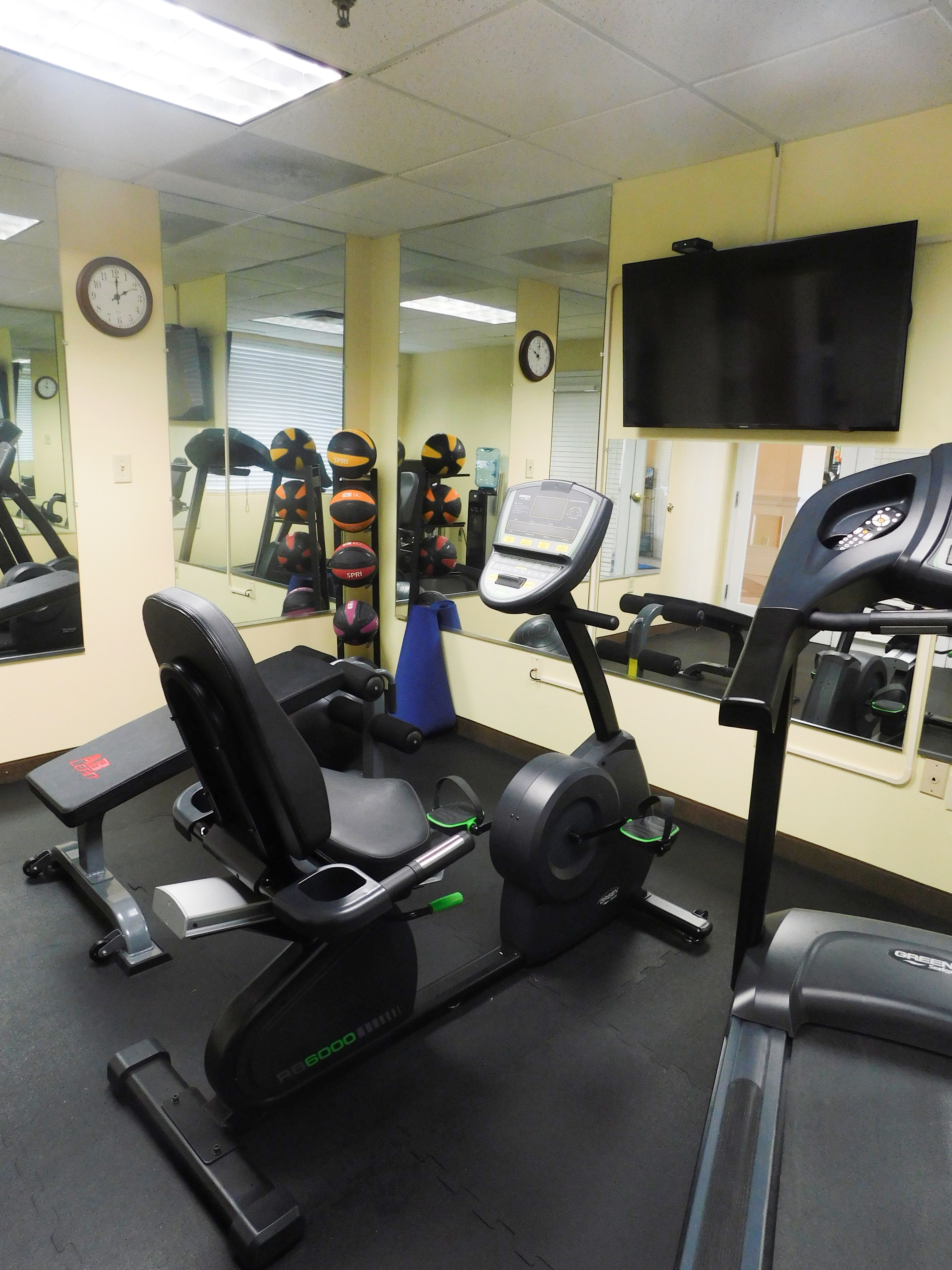 A gym with exercise equipment, including treadmills and a stationary bike, and mirrors on the walls.