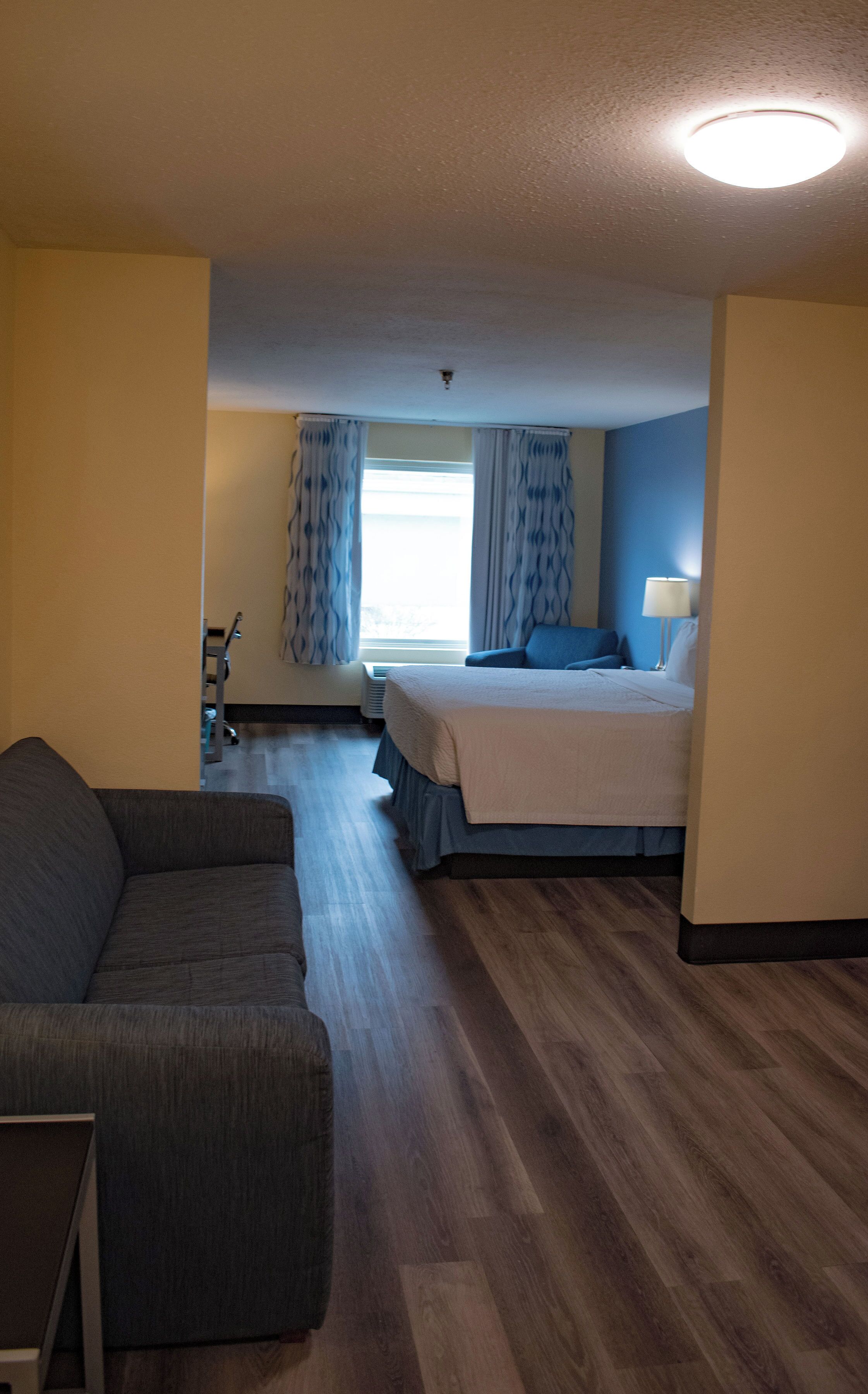 Habitación de hotel con cama, sofá, ventana con cortinas, lámpara de techo y radiador.
