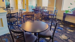 Un comedor de hotel con mesas y sillas redondas, una alfombra estampada y un candelabro.