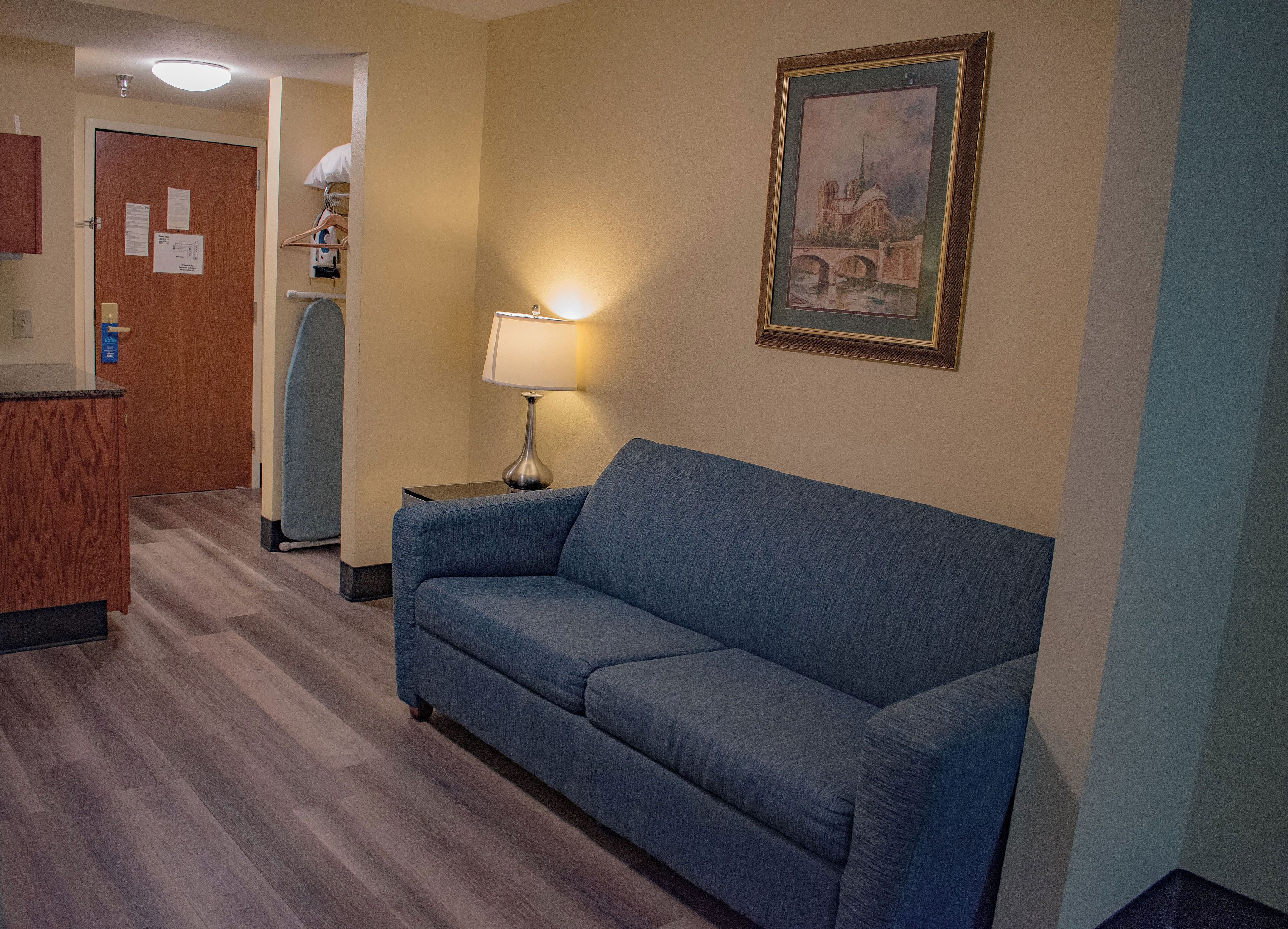 Habitación de hotel con un sofá azul, una lámpara, un cuadro y un escritorio de madera.
