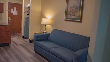 Habitación de hotel con un sofá azul, una lámpara, un cuadro y un escritorio de madera.