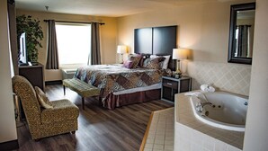 Habitación de hotel con cama, zona de estar con una silla, escritorio, lámpara, espejo grande y bañera.