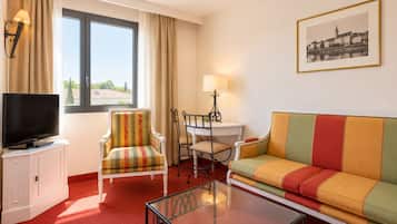Una habitación de hotel con televisión, un sofá, una silla, una mesita y una ventana con cortinas.