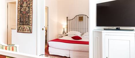 A hotel room with a bed, a television, a nightstand, a lamp, and a tapestry on the wall.
