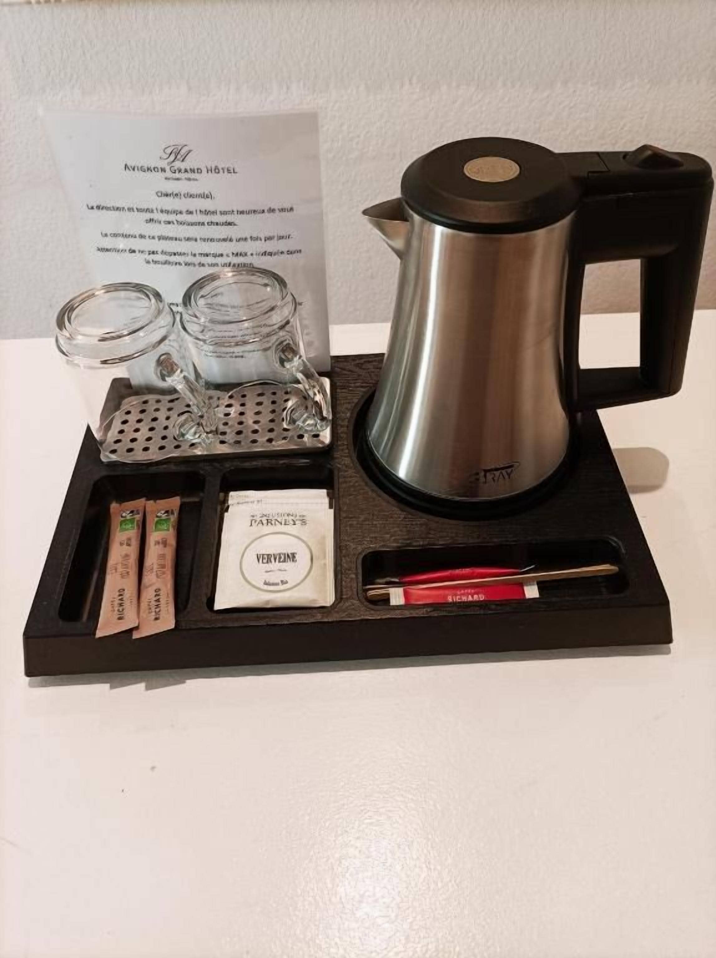 Una cafetera, dos recipientes de vidrio, un sobre de azúcar, un sobre de crema y una cuchara sobre una bandeja.