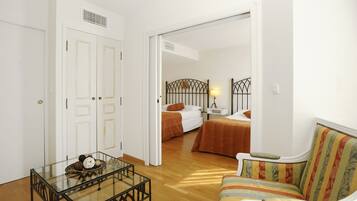 A room with a glass table, a sofa, two beds with orange bedding, and a white door.