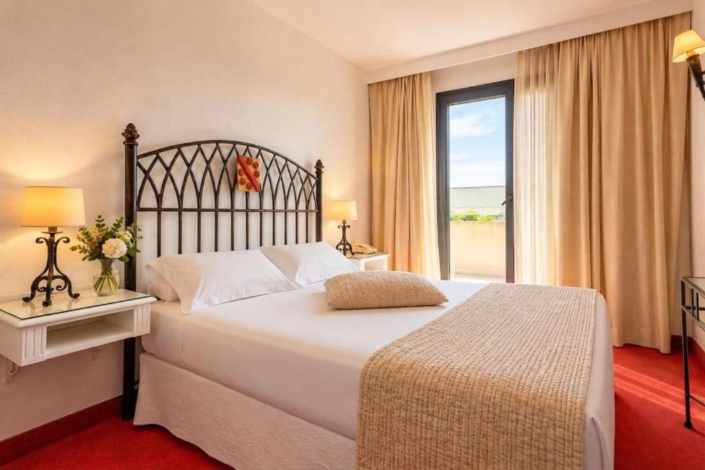 A hotel room with a bed, bedside tables, lamps, and a view of the outdoors.