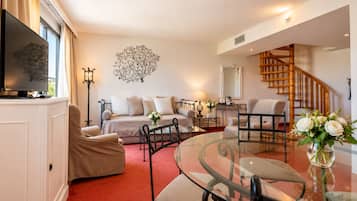 A modern living room with a sofa, armchairs, a glass coffee table, a TV, and a decorative tree wall art.