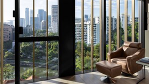 Een moderne kamer met een groot raam dat uitzicht geeft op de stad, een bruine leren fauteuil en een klein tafeltje.