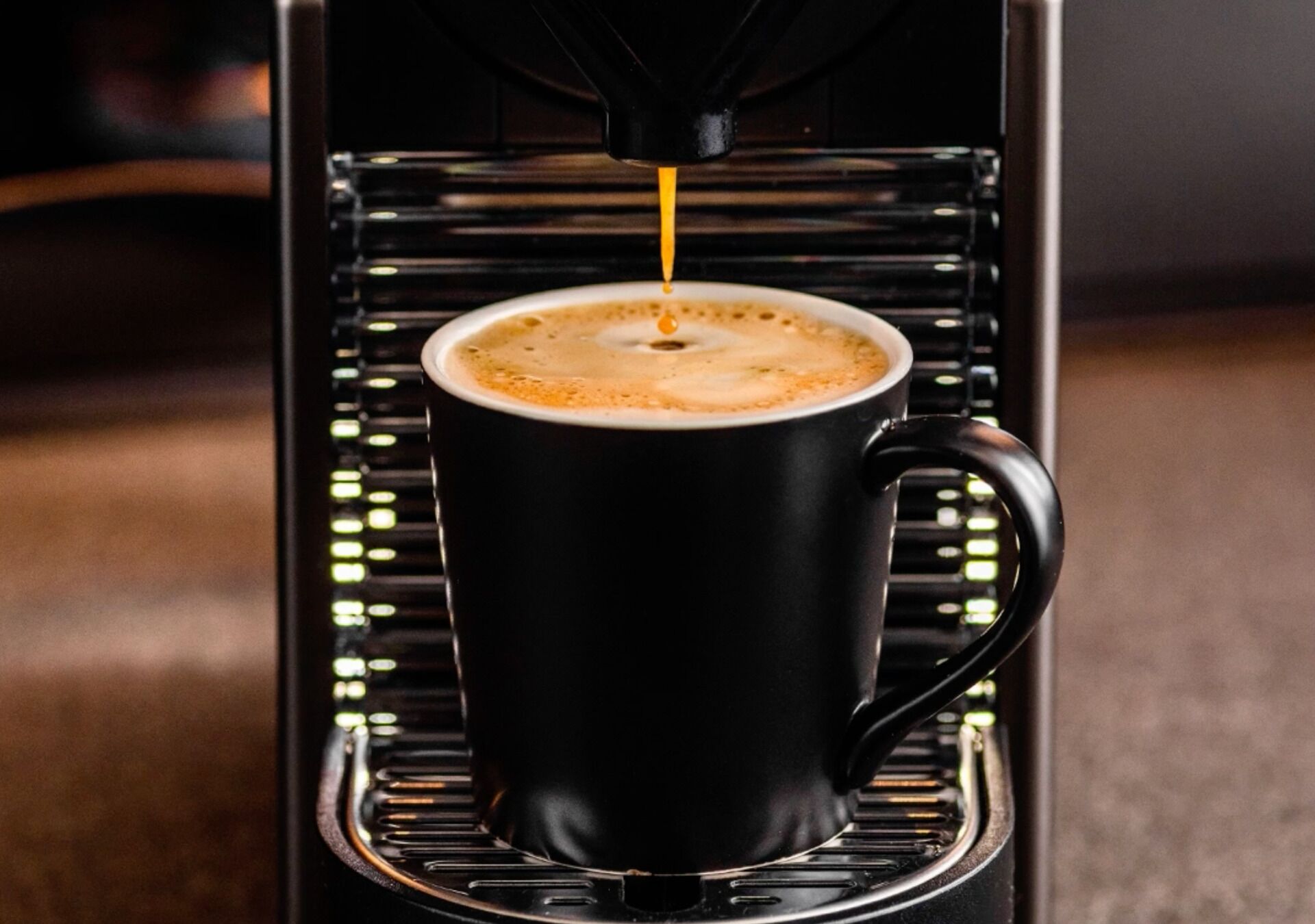 Une tasse à café noire est posée sur une machine à café, et on peut clairement voir le café être versé.