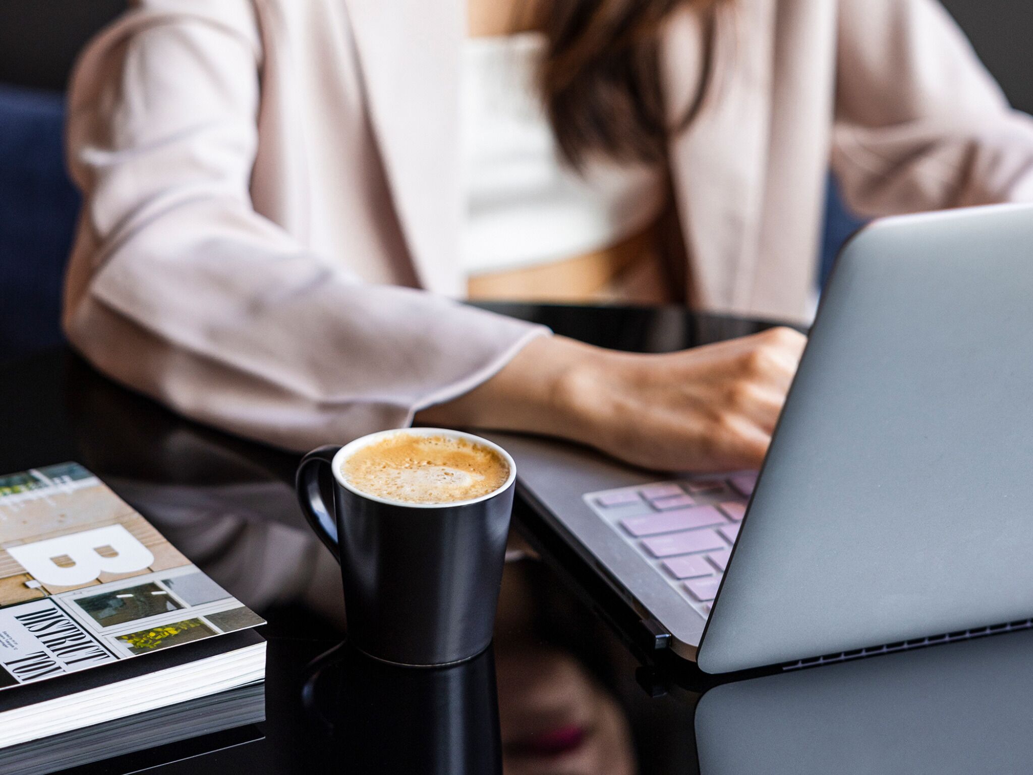 Una persona trabajando en un ordenador portátil con una taza de café sobre la mesa.