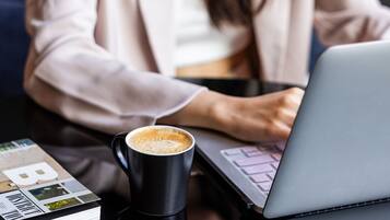 Una persona trabajando en un ordenador portátil con una taza de café sobre la mesa.